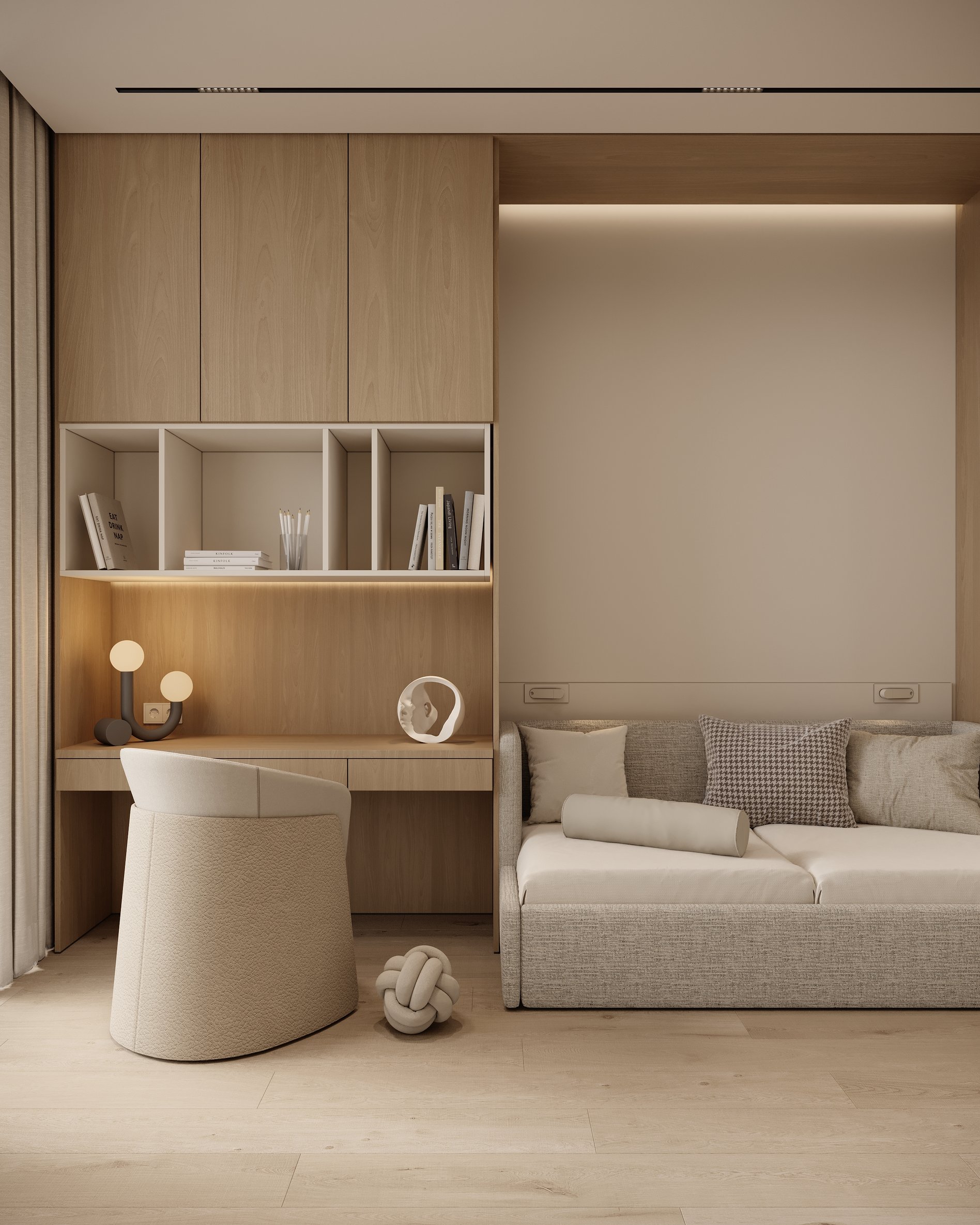 Minimalist study nook with built-in desk, open shelving, and a neutral armchair, next to a sofa with textured pillows.