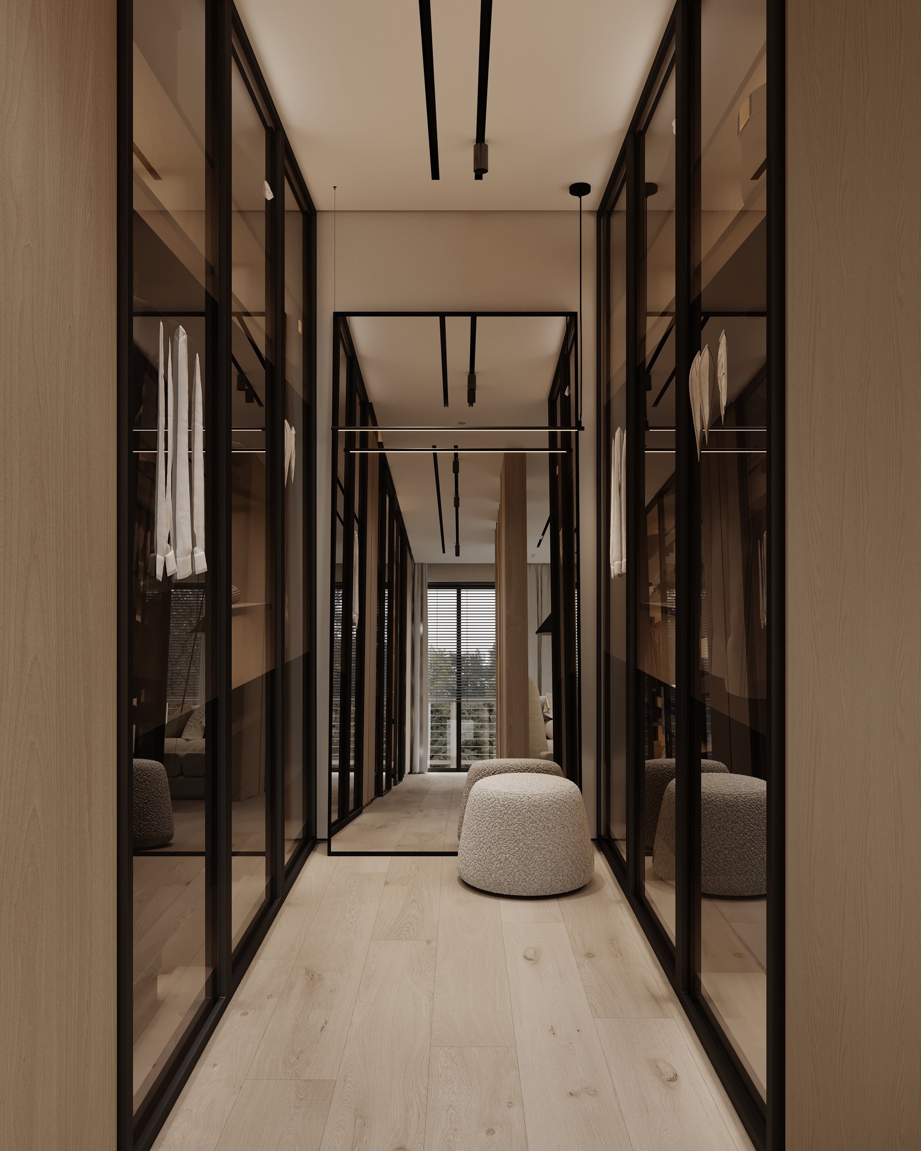 Modern walk-in closet with glass-fronted wardrobes, black metal frames, and soft ottoman seating, leading to a bright window view.