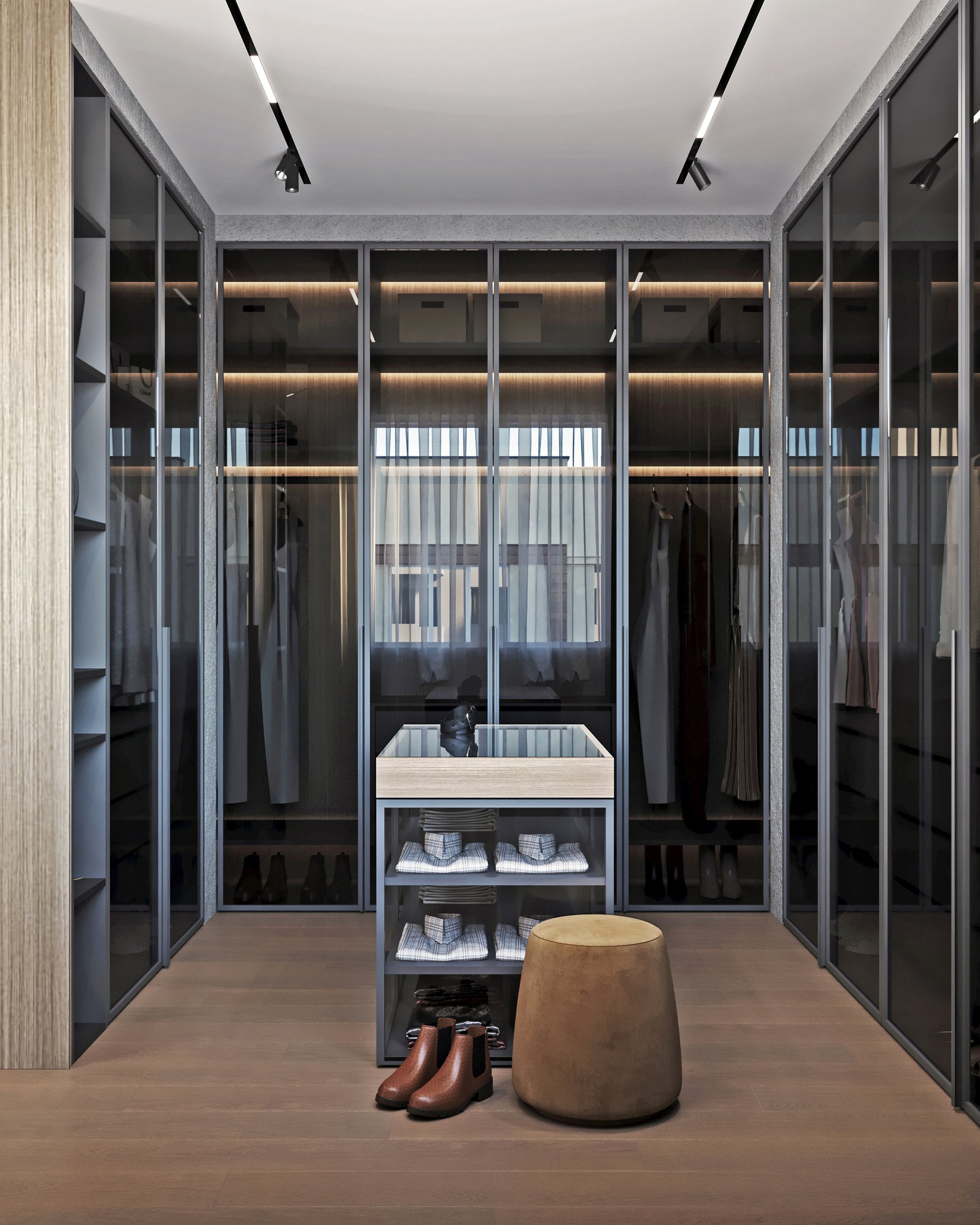 Walk-in closet with illuminated glass cabinets, folded clothing storage, and leather ottoman with brown leather boots displayed.